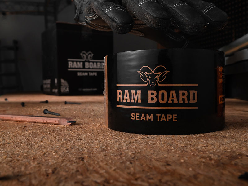close up of a roll of package ram board seam tape in the foreground. Pencil, screws and box of tape sit in the background
