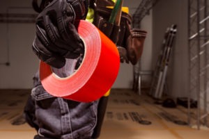 Close up of a gloved hand holding a roll of red Pro tape duct tape