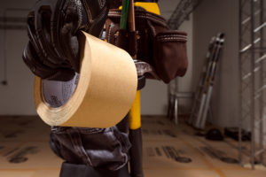 close up view of a gloved hand holding a roll of brown ram board seam tape