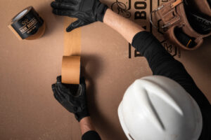 top down view of brown ram board seam tape being applied to floor protection sheets by a man in a hard hat.